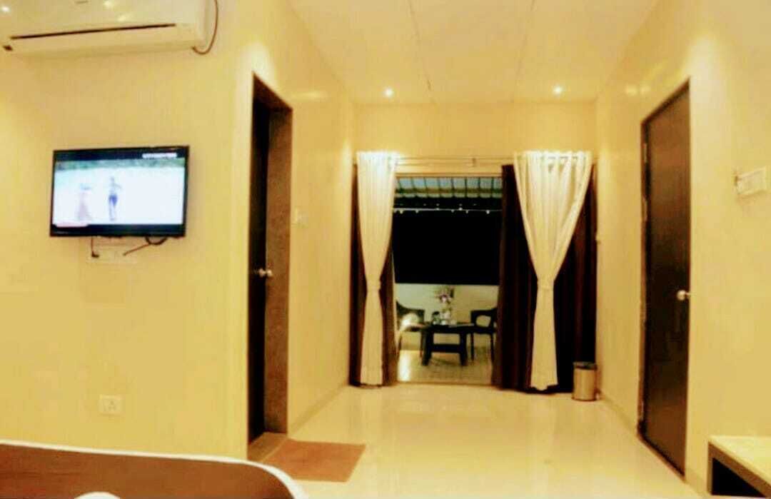 A hotel room with a television mounted on the wall, a door leading to a dining area, and a small table with chairs.