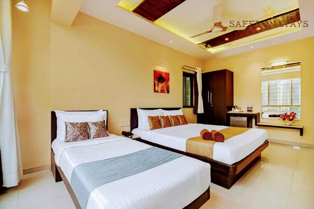 A hotel room with two beds, a ceiling fan, a window with blinds, and a small table with a vase of flowers.