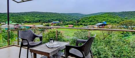 A balcony with a table and chairs, overlooking a lush green landscape.
