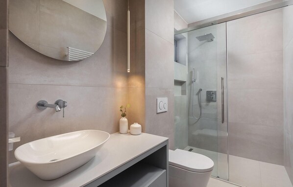 A modern bathroom with a large white sink, a glass shower enclosure, and a minimalist design.