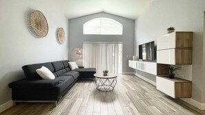 A modern living room with a sectional sofa, a round coffee table, and a TV mounted on a white cabinet. - Behemian 4Bd Villa w/ Pool at Solana Resort (Davenport)