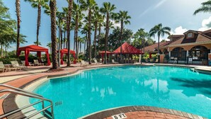 A swimming pool surrounded by palm trees and red canopies, with a brick walkway and a building in the background. - Behemian 4Bd Villa w/ Pool at Solana Resort (Davenport)