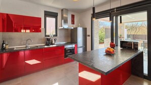 A modern kitchen with red cabinetry, a stainless steel refrigerator, a built-in oven, and a microwave. There is a large window providing a view of the outdoors. - Stunning home in Svetvincenat (Svetvincenat)