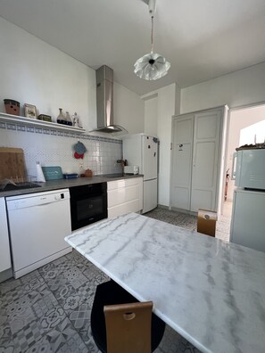 Ett modernt kök med vita skåp, en diskmaskin från Bosch, en bänkskiva i marmor och en hängande lampa.