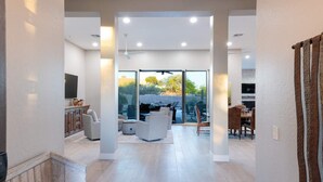 A spacious living area with a large sliding glass door leading to an outdoor patio, a kitchen area, and a seating area with a sofa and chairs. - Luxury Retreat with Heated Pool in Scottsdale (Scottsdale)