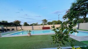 A swimming pool with a surrounding grassy area and a paved walkway. - Boalotswe Inn (Maun)
