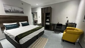 A modern hotel room with a large bed, a desk, a chair, and a wardrobe. - Boalotswe Inn (Maun)