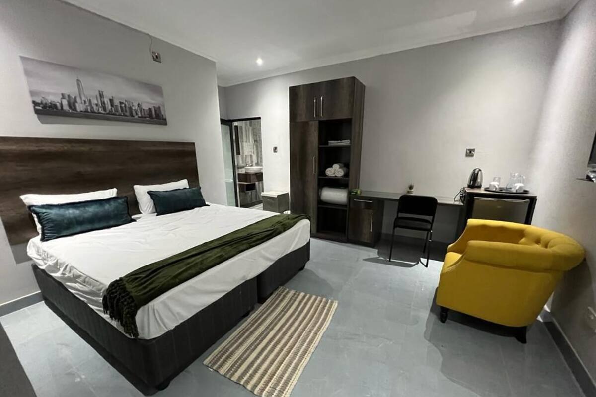 A modern hotel room with a large bed, a desk, a chair, and a wardrobe.