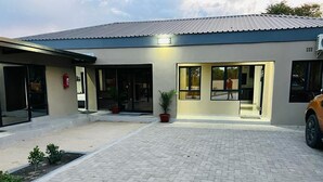 A modern building with a paved courtyard, large windows, and a car parked outside. - Boalotswe Inn (Maun)