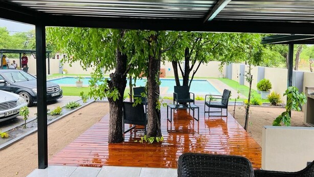 An outdoor patio with a covered seating area, a pool, and a view of a residential street. - Boalotswe Inn (Maun)