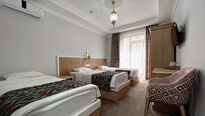 A hotel room with two beds, a chair, a desk, and a television. - SHAHEREZADE GARDEN (Bukhara)