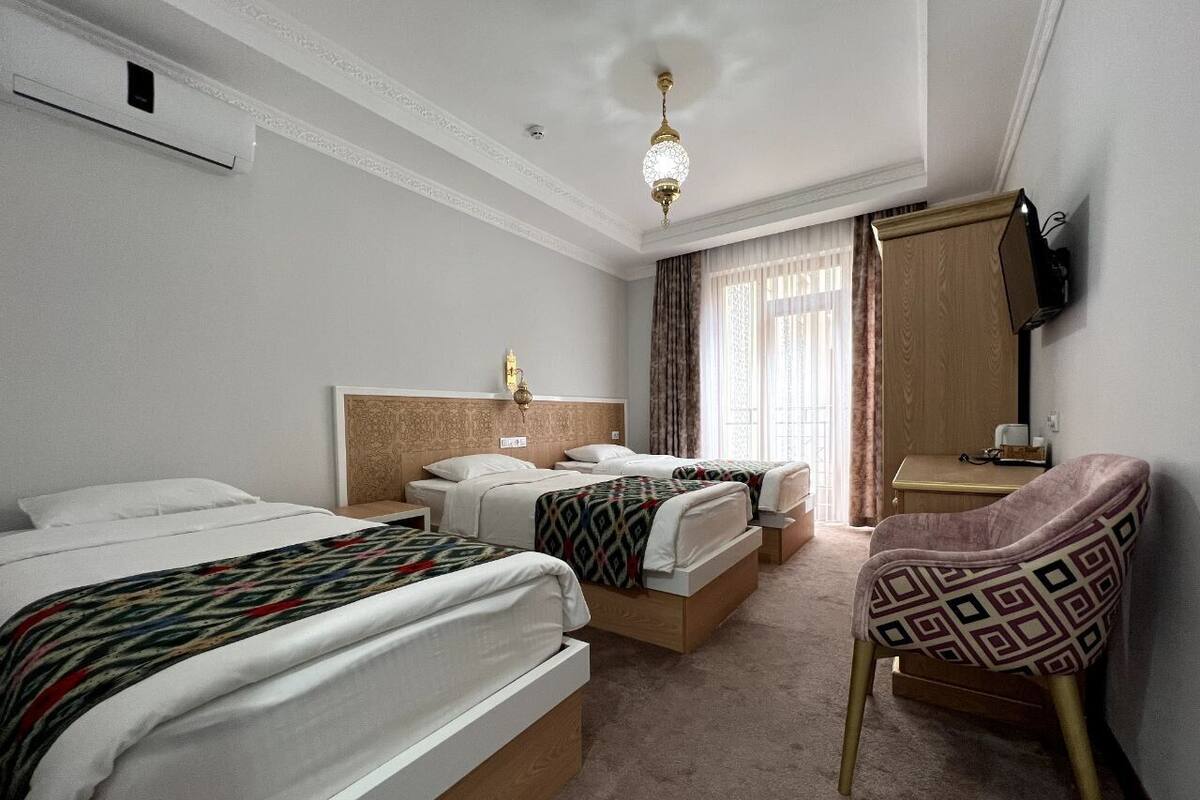 A hotel room with two beds, a chair, a desk, and a television.