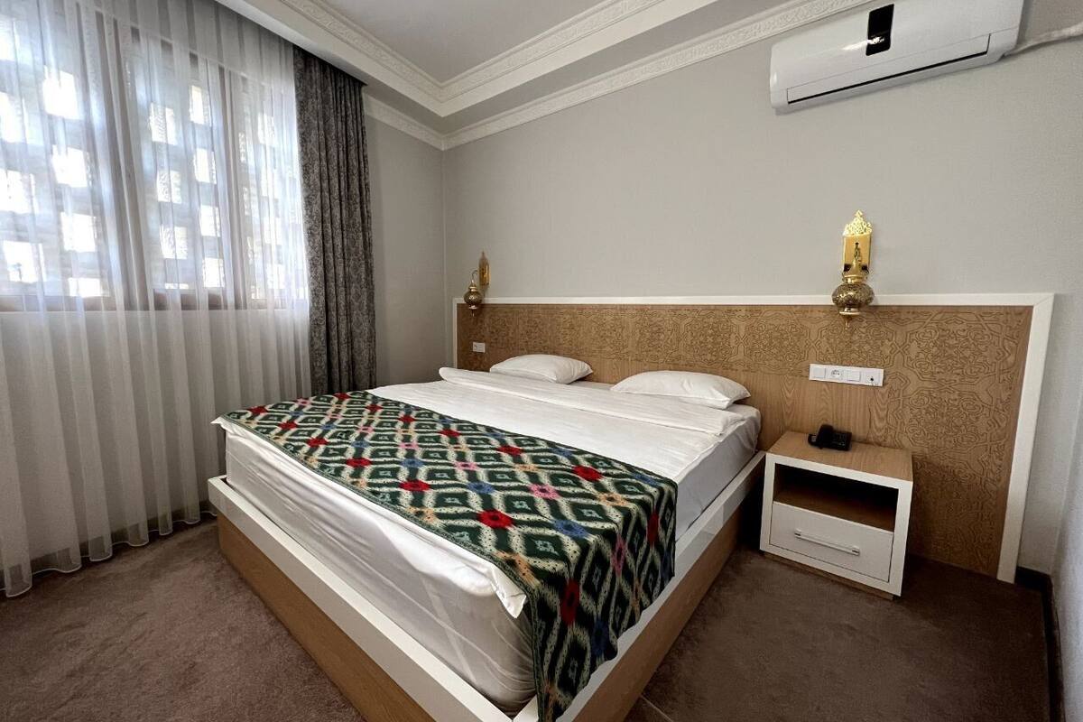 A hotel room with a bed, a nightstand, a lamp, and an air conditioning unit.
