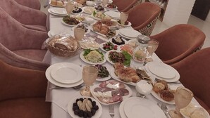 A dining area with a long table set for a meal, surrounded by cushioned chairs. - SHAHEREZADE GARDEN (Bukhara)