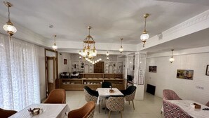 A dining area with a central table, surrounded by patterned chairs, and a chandelier overhead. - SHAHEREZADE GARDEN (Bukhara)