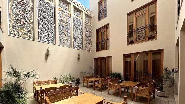 A courtyard with wooden tables and chairs, potted plants, and decorative screens. - SHAHEREZADE GARDEN (Bukhara)