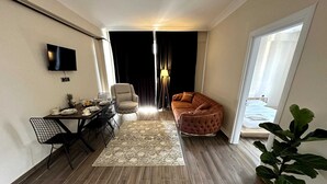 A modern living room with a dining area, a flat-screen TV mounted on the wall, a sofa, and a potted plant. - CAPPADOCIA SUIT RESIDENCE (Nevsehir)