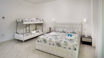 Una habitación con una cama litera y una cama individual, ambas con ropa de cama floral. Hay una mesita de noche con una lámpara y un pequeño objeto decorativo.