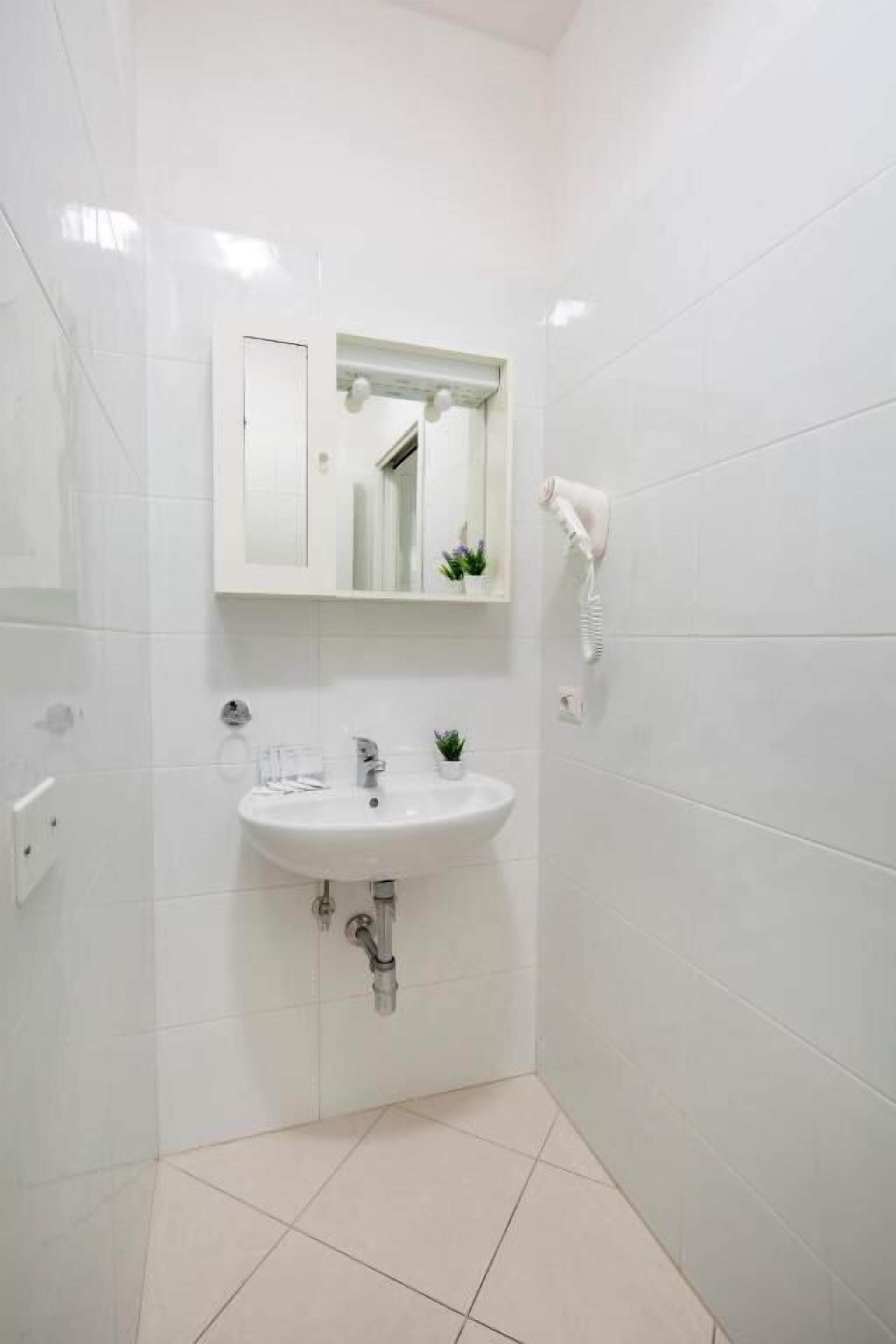 Un baño con azulejos blancos, un lavamanos, un espejo y un secador de pelo.