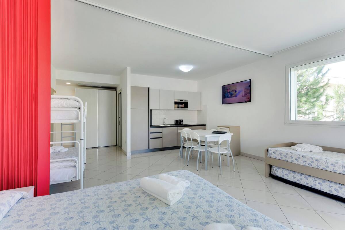 A modern hotel room with bunk beds, a kitchenette, a dining area, and a large window.