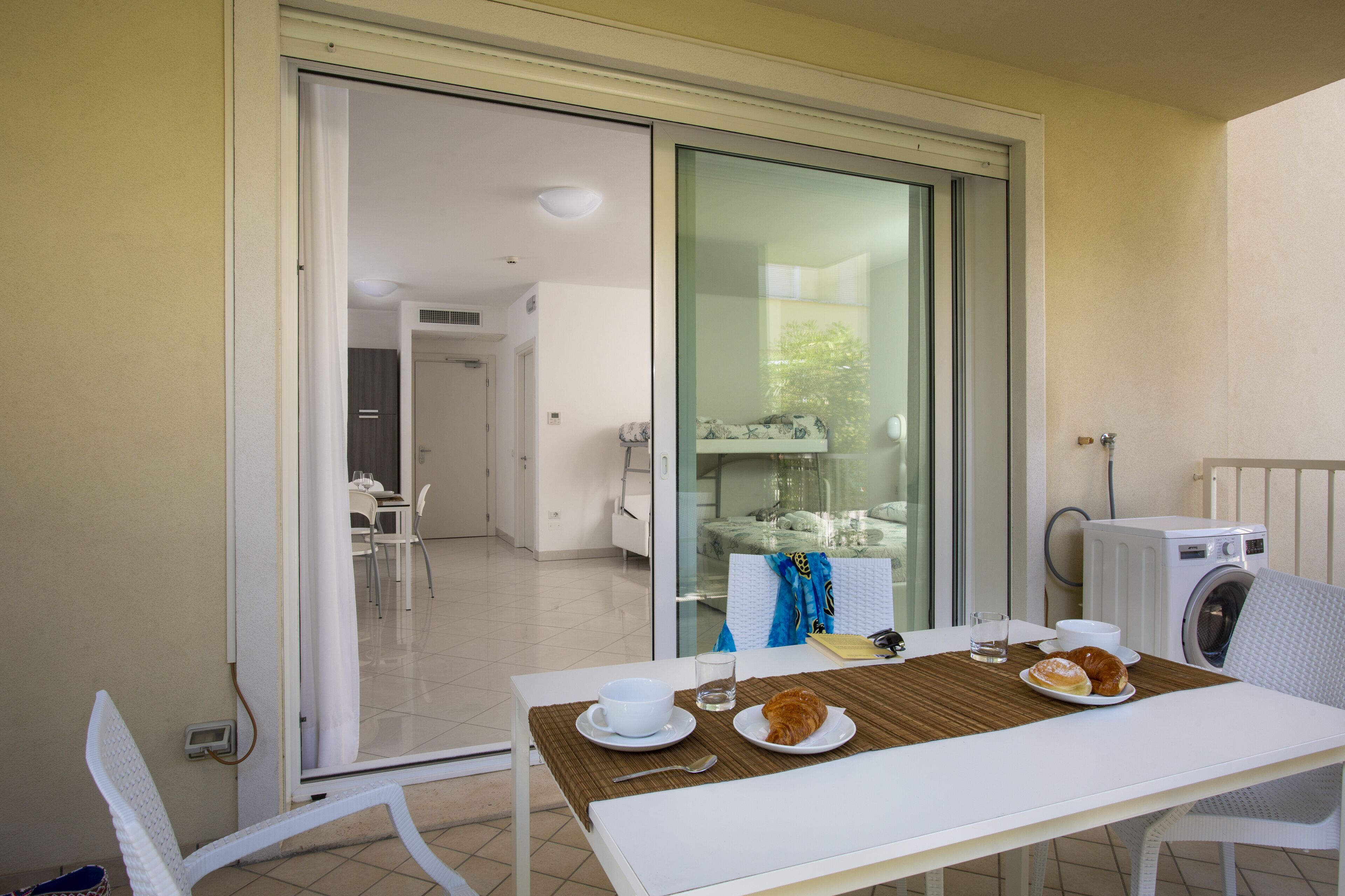 A dining area with a table set for two, a washing machine, and a sliding glass door leading to a balcony.