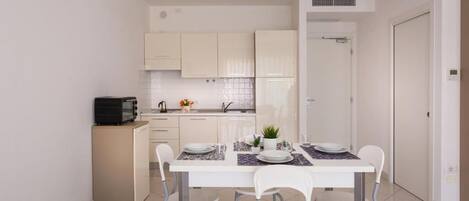 A compact kitchen with white cabinets, a dining table set for four, and a small refrigerator.