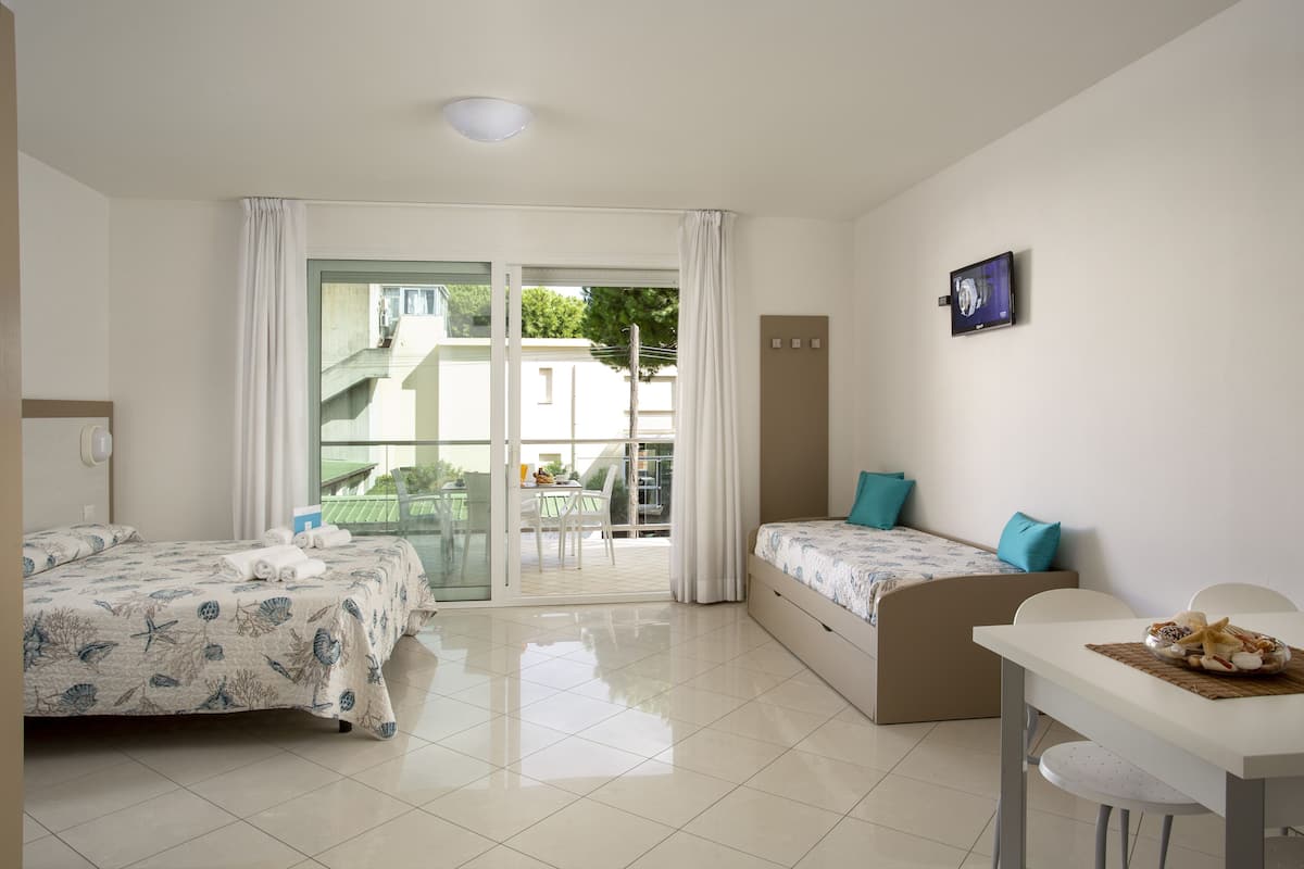 A hotel room with two beds, a dining table, and a sliding glass door leading to a balcony.