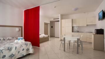 Una habitación de hotel con cama, una mesa de comedor con sillas, una cocina y un separador rojo.