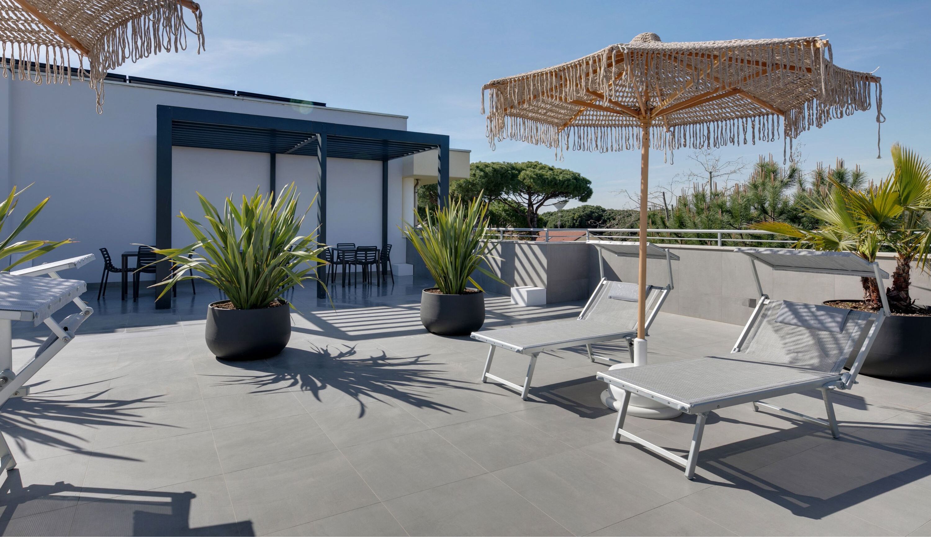 A rooftop terrace with outdoor seating, potted plants, and a woven umbrella.