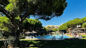 Un espace piscine agrémenté de chaises longues et de parasols, entouré d’arbres et d’immeubles.