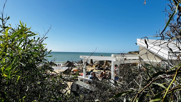 Une plage avec vue sur un kiosque blanc, des parasols en chaume et des gens qui se détendent.