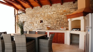 An outdoor kitchen with stone walls, wicker furniture, and a built-in oven. - Beautiful home in Kanfanar with sauna (Kanfanar)