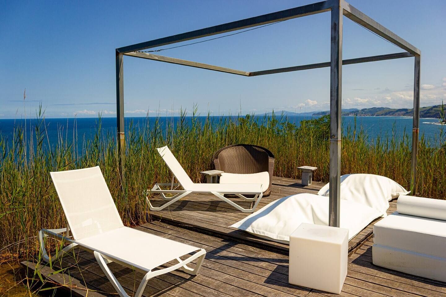 Een houten terras met witte lounge stoelen en een overdekte zithoek met uitzicht op een waterpartij.
