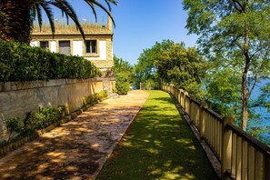 A pathway leading to a building with a stone facade, bordered by a wooden fence and lush greenery.
