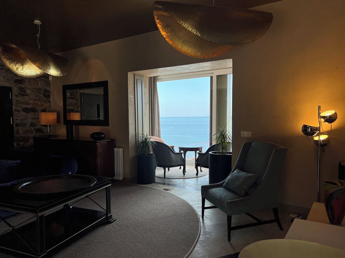 A living room with a view of the sea, a fireplace, and a large window.