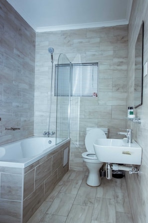 A modern bathroom with a bathtub, toilet, and sink. - SESIGO BED AND BREAKFAST (Ghanzi)