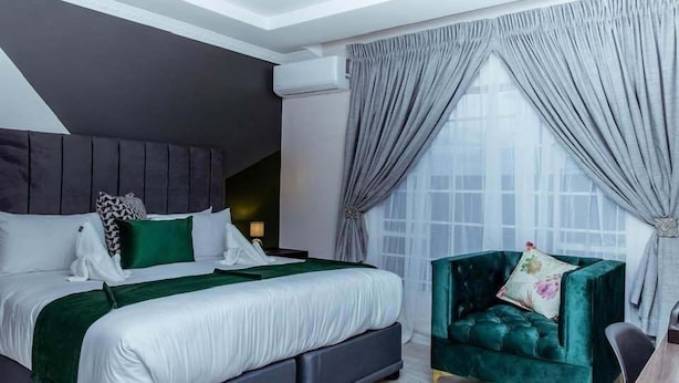 Une chambre moderne avec un grand lit, une tête de lit sombre et un fauteuil vert.