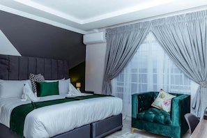 A modern bedroom with a large bed, a dark headboard, and a green armchair. - SESIGO BED AND BREAKFAST (Ghanzi)