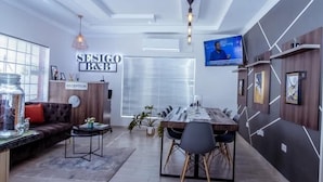 Un espace d’accueil moderne comprenant un comptoir de réception, un canapé et un coin repas avec une longue table et des chaises.