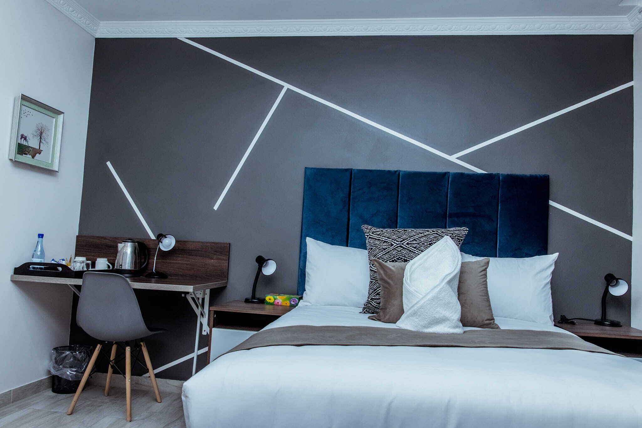 Et moderne hotelværelse med en pænt redt seng, et skrivebord med stol og et natbord med lampe.