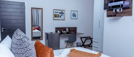 A modern hotel room with a bed, a desk, a chair, a TV, and artwork on the walls.