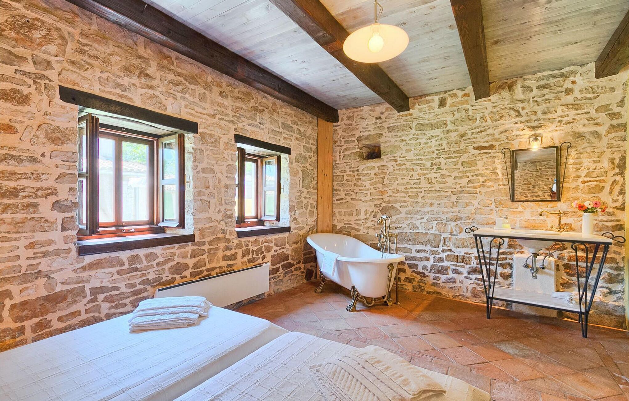 Ein rustikales Badezimmer mit Steinwänden, einer freistehenden Badewanne und einem alten Waschbecken.