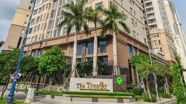 A high-rise hotel with multiple floors, a prominent entrance, and a landscaped area with palm trees. - Macy Apartment - Tresor Sai Gon Downtown (Ho Chi Minh City)