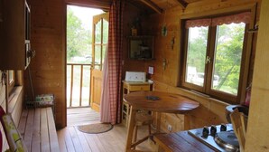 Een gezellig houten vakantiehuisje met een eethoek, tafel en stoelen, een keuken met fornuis, en een groot raam met uitzicht op de natuur.