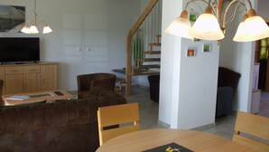 Ein Essbereich mit Holztisch und Stühlen, einem Fernseher auf einer Kommode und einer Treppe im Hintergrund.