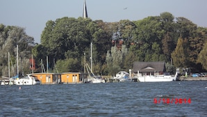 Ein Anwesen am Wasser mit einem Steg, Booten und einem Kirchturm im Hintergrund.