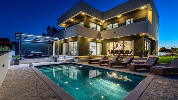 Una casa moderna de dos pisos con piscina, mobiliario exterior y un porche cubierto.