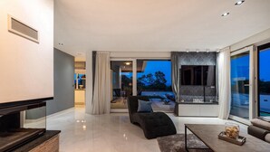 Una sala de estar moderna con una televisión de pantalla plana, un sofá, una mesa de centro y vistas al exterior.