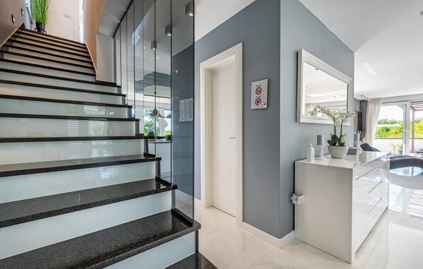 Un intérieur moderne avec un escalier en verre, une salle de bain dotée d’un lavabo et d’un miroir, et une porte sur laquelle est apposé un panneau « interdiction de fumer ».