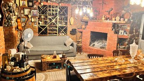 A cozy room with a brick fireplace, a herringbone-patterned sofa, a wooden dining table, and a barrel of liquor.